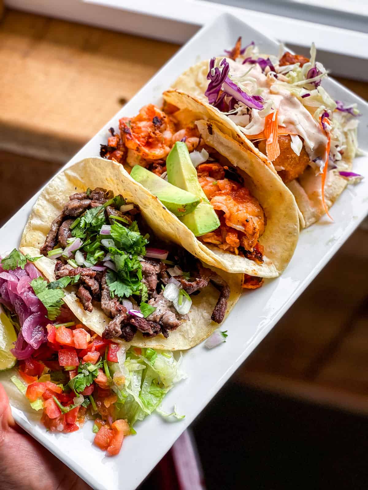 Straight down view of four tacos on a rectangular white plate.