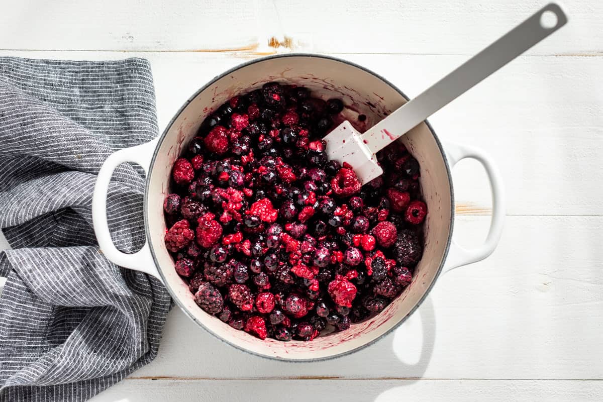 Frozen berries being mixed into the maple syrup and tapioca starch in a large white pot.