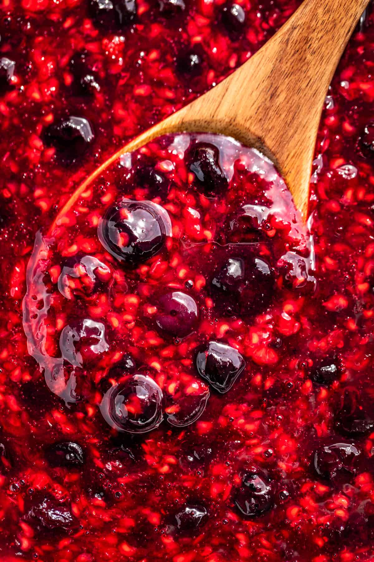 Close macro view of berry sauce being scooped out with a wooden spoon.