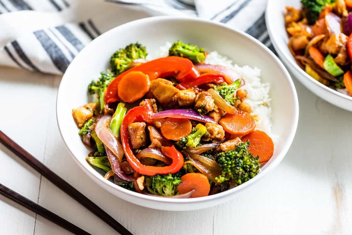 Two white bowls of Chicken Stir Fry with chopsticks next to the front bowl.