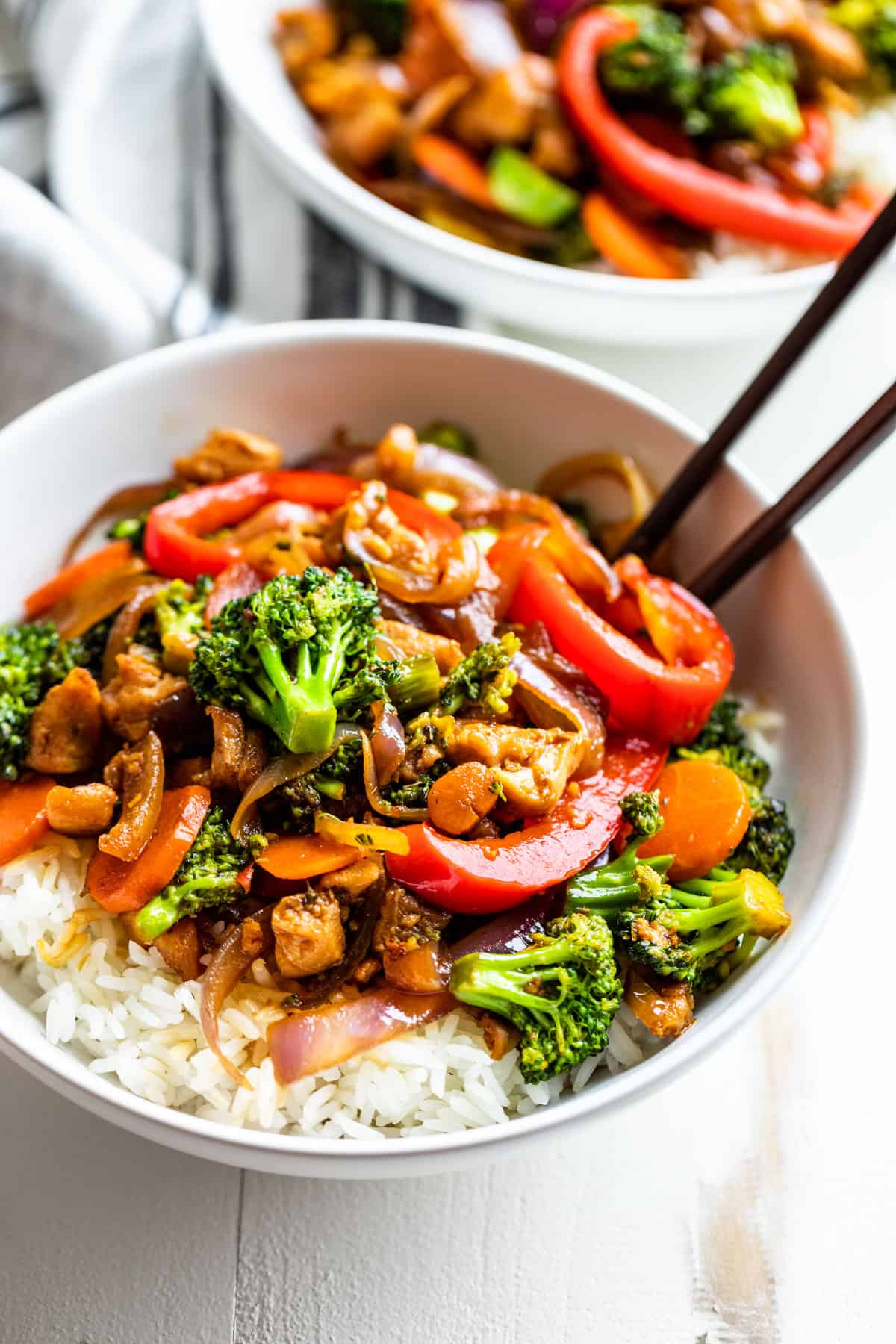 Side view of two bowls filled with rice and topped with Chicken Stir Fry with a pair of chopsticks on the side.