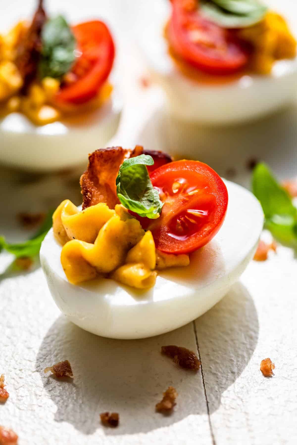 Three BLT deviled eggs with bacon bits around them on a white background.