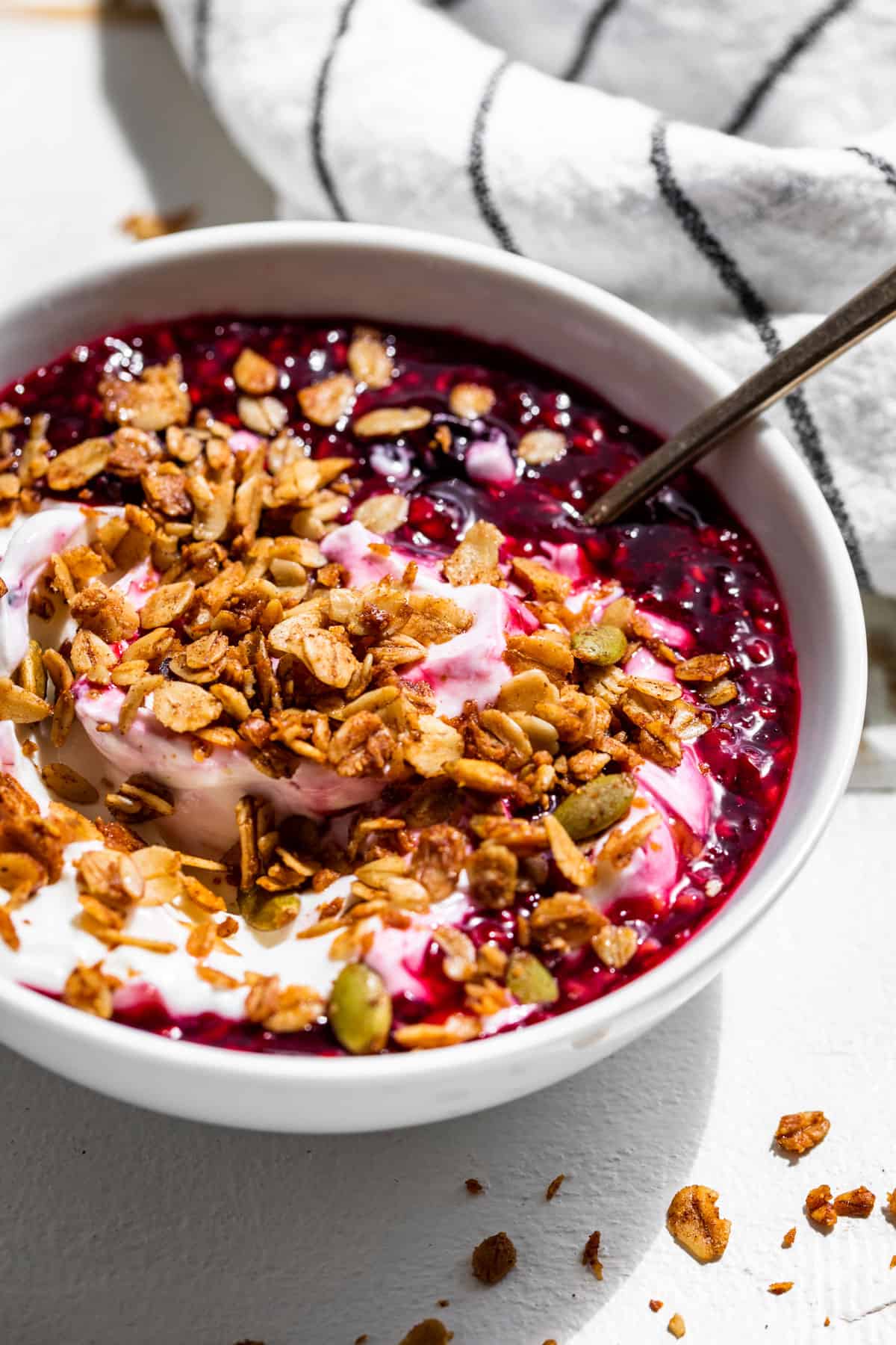 Yogurt with Berry Sauce and Homemade Granola in a white bowl.