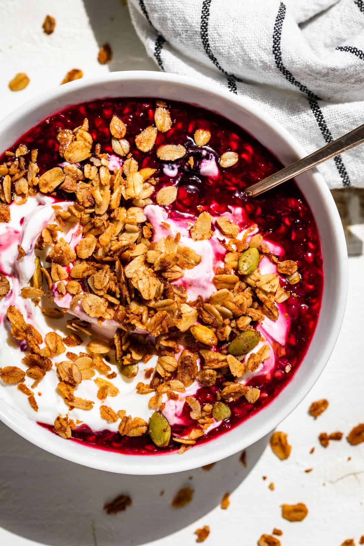 A white bowl with yogurt, berry sauce, and granola.