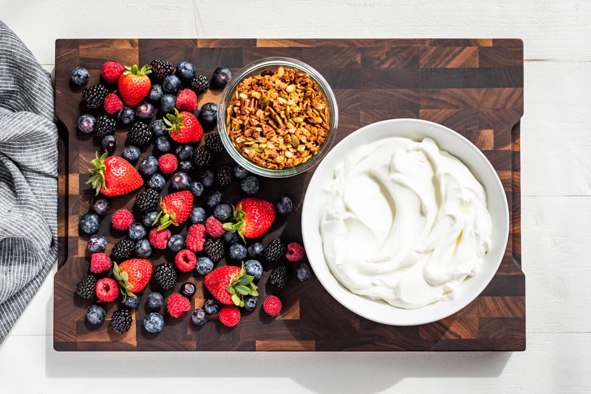 Yogurt, fresh fruit, and granola on a wood cutting board.