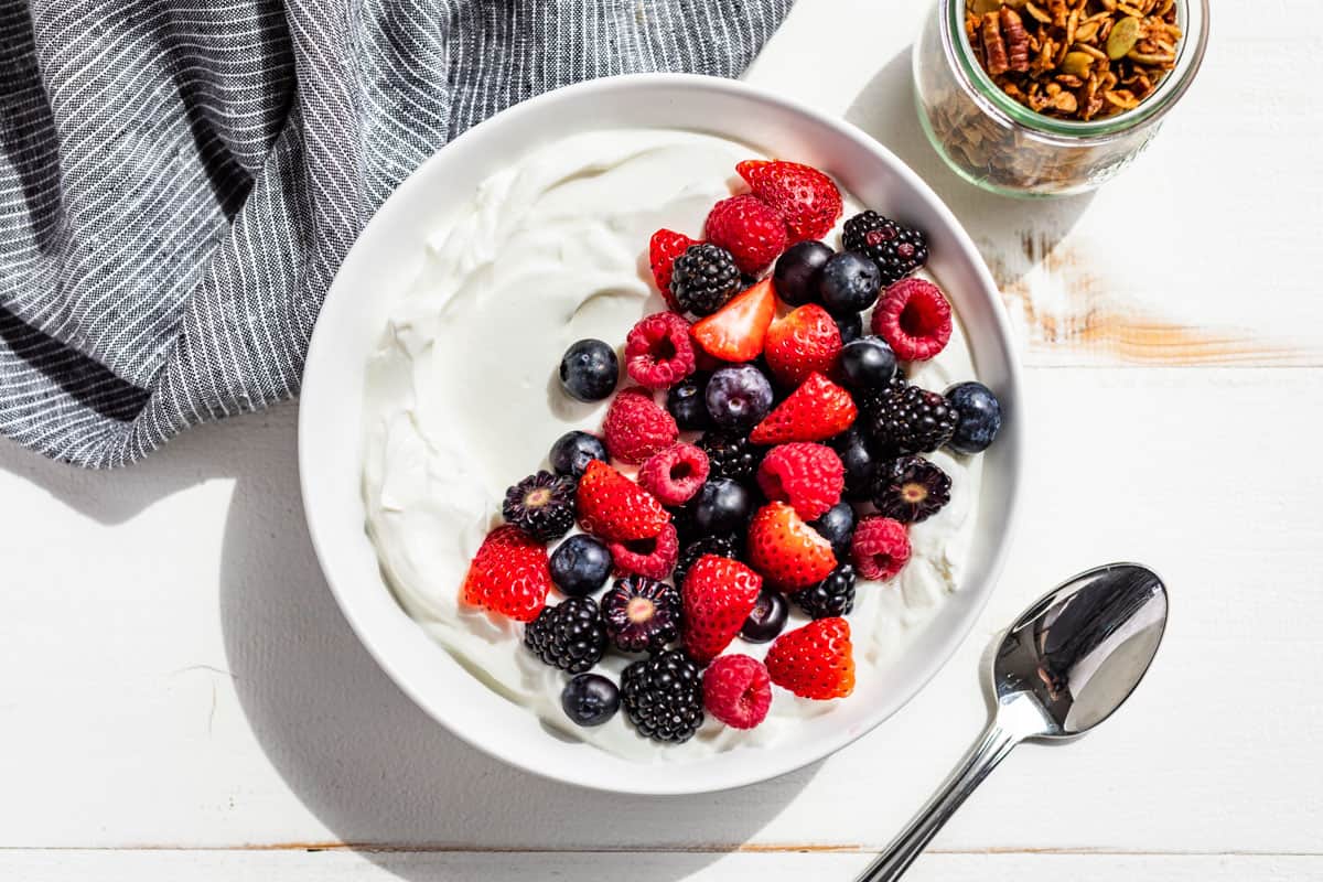 Yogurt in a white bowl topped with fresh berries and granola on the side.