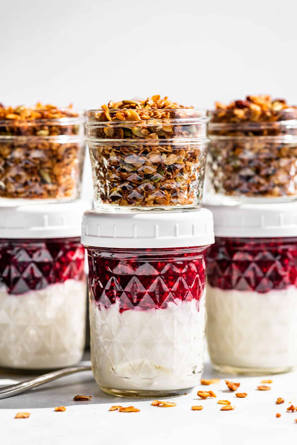 Glass jars with yogurt and berry sauce with small jars of granola on the side.