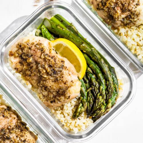 Three glass containers with Garlic Herb Chicken and Asparagus topped with lemon wedges on a white background.