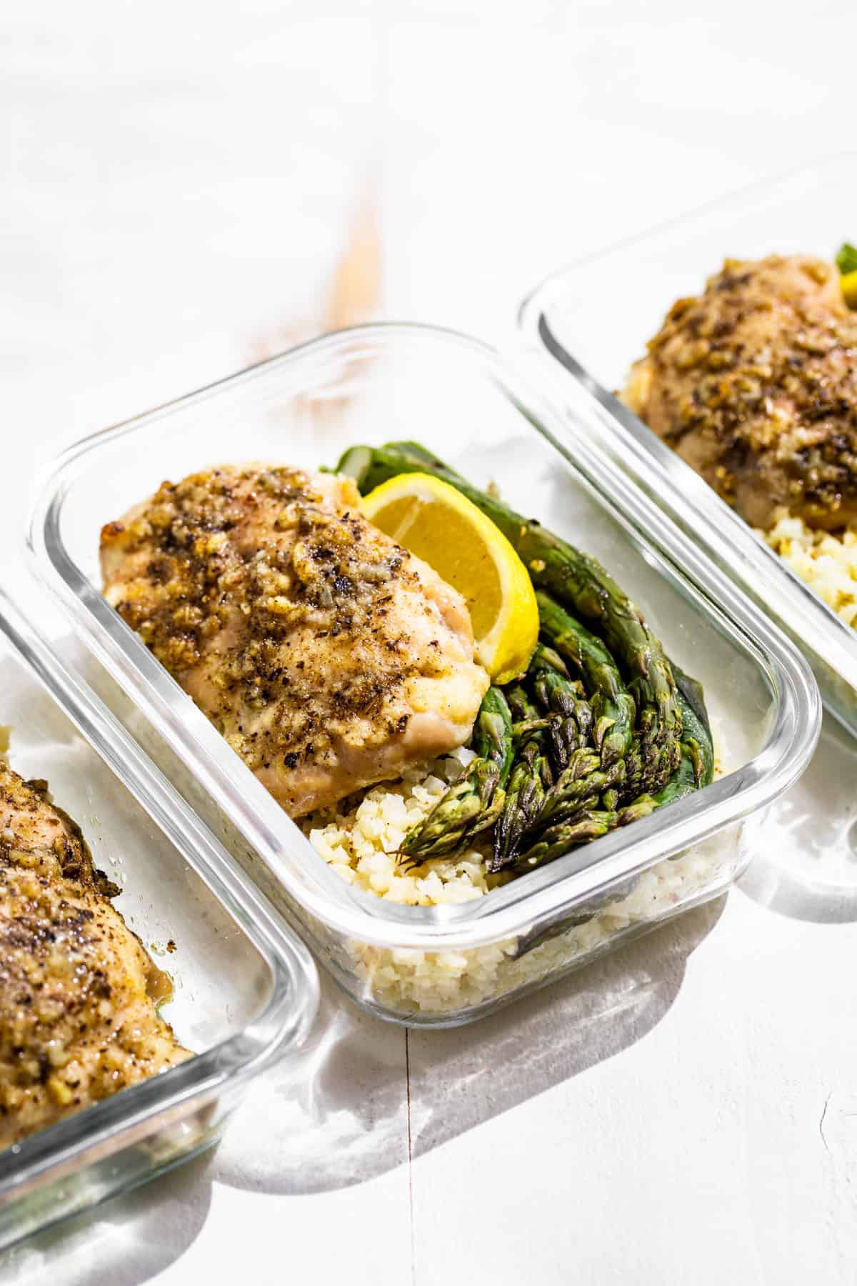 Garlic Herb Chicken thigh over cauliflower rice with asparagus on the side topped with a lemon wedge.