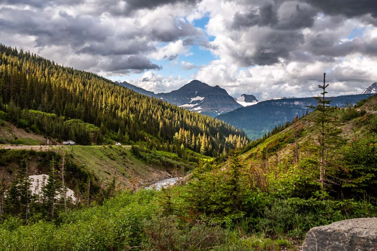 View of the mountains with trees in the foreground with Going to the Sun Road in the distance.