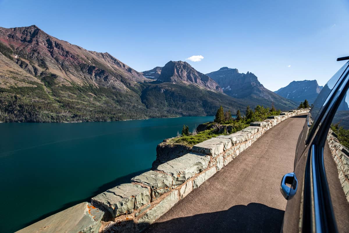 View over St. Mary Lake with mountains in the background and the Going to the Sun Road in the foreground with a black truck parked in the pull off.