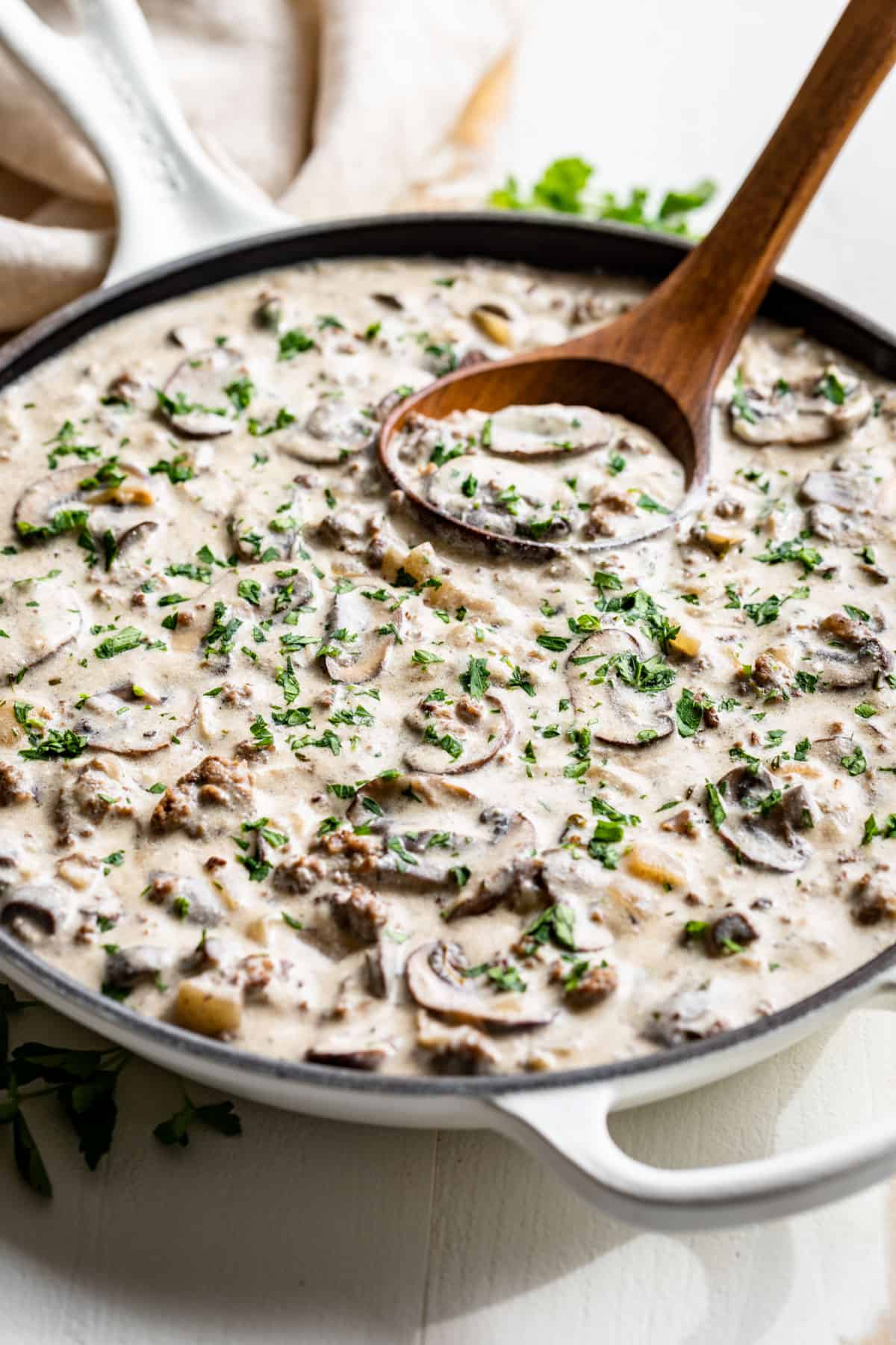 Side view of a white skillet full of Ground Beef Stroganoff with a wooden ladle.