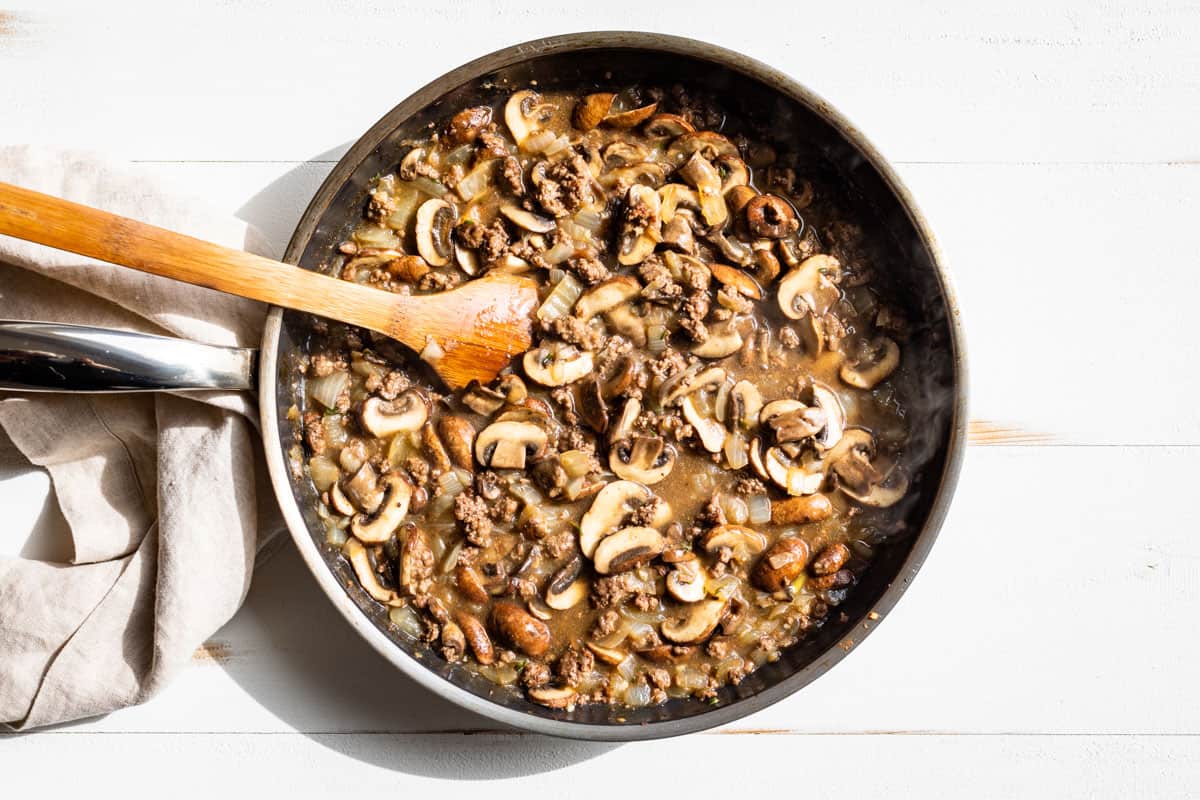Adding the beef broth to the skillet with the ground beef and mushrooms.