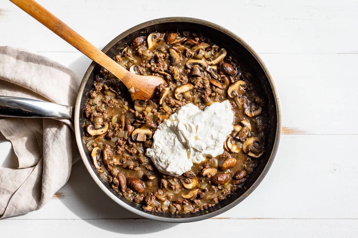 Adding the sour cream as the final step to the ground beef stroganoff.