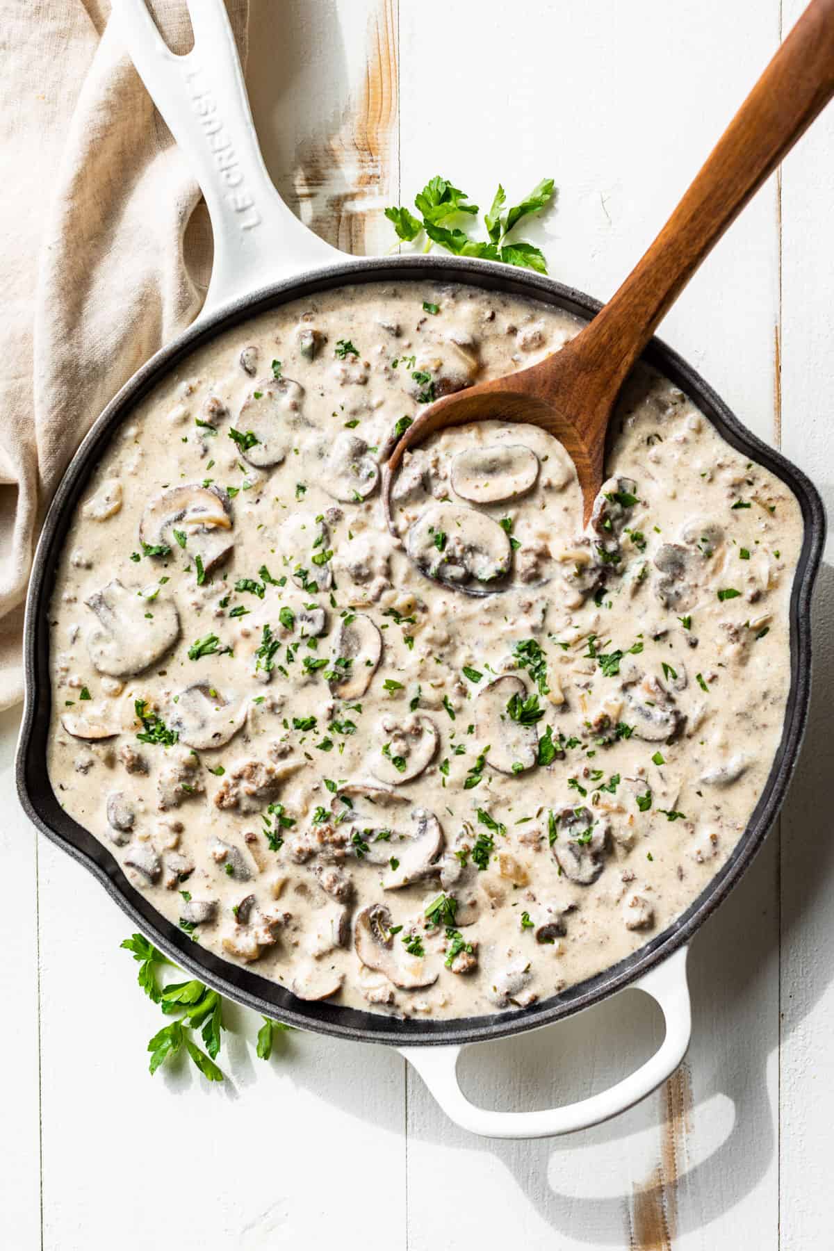 Straight down view of finished Ground Beef Stroganoff in a white skillet with a wooden ladle scooping some out.