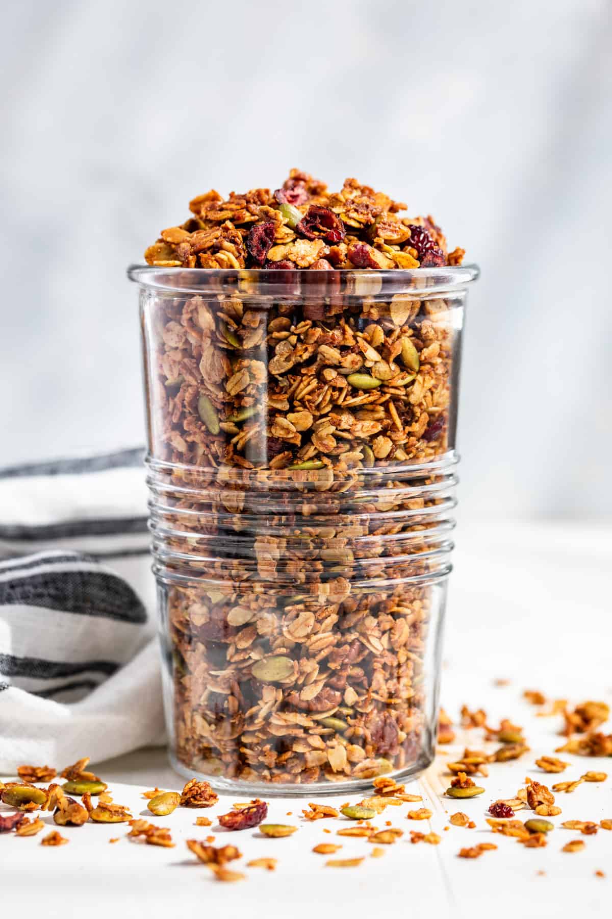 A large clear glass jar filled with Homemade Granola with a blue background.