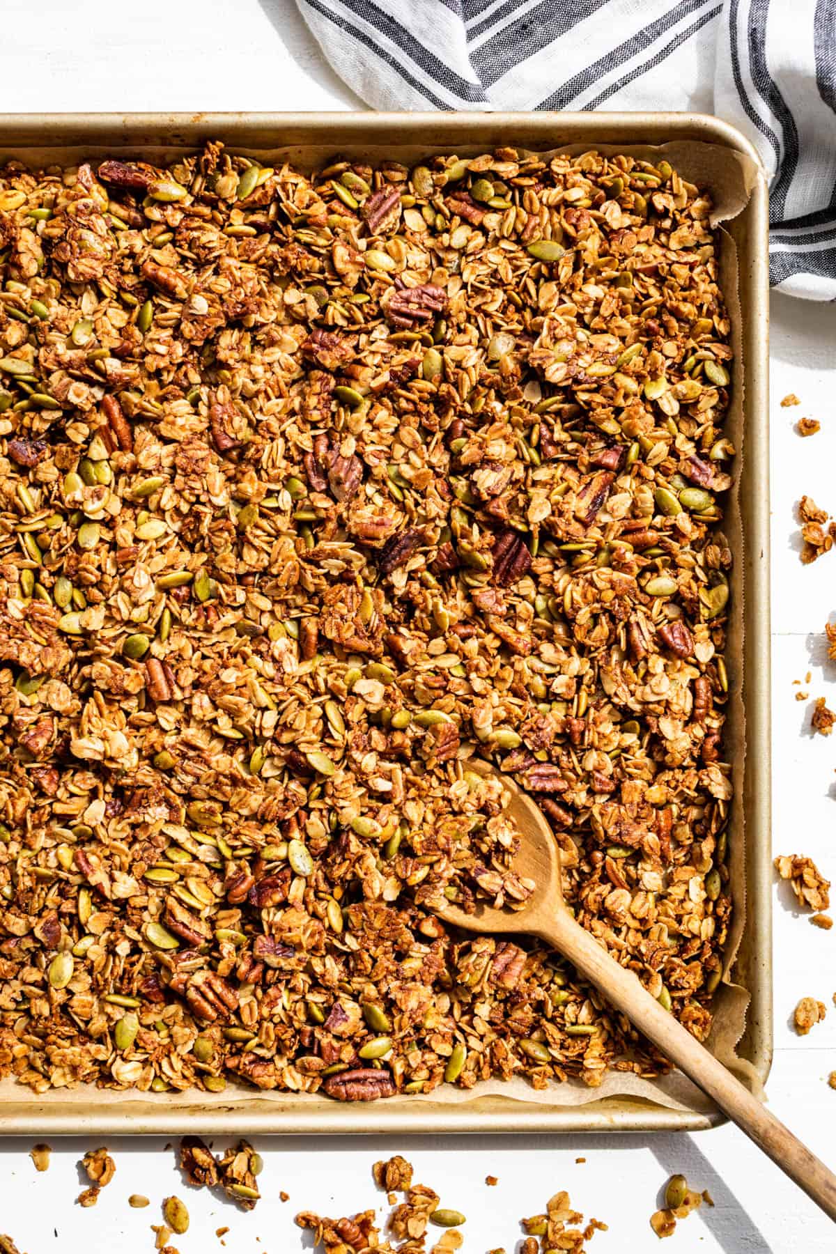 Straight down view of a sheet pan filled with granola and a wooden spoon.