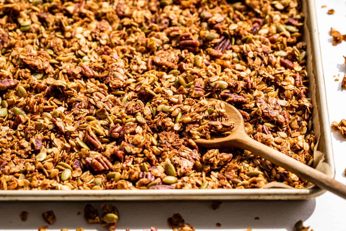 Side view of baked granola in a baking sheet with a wooden spoon.