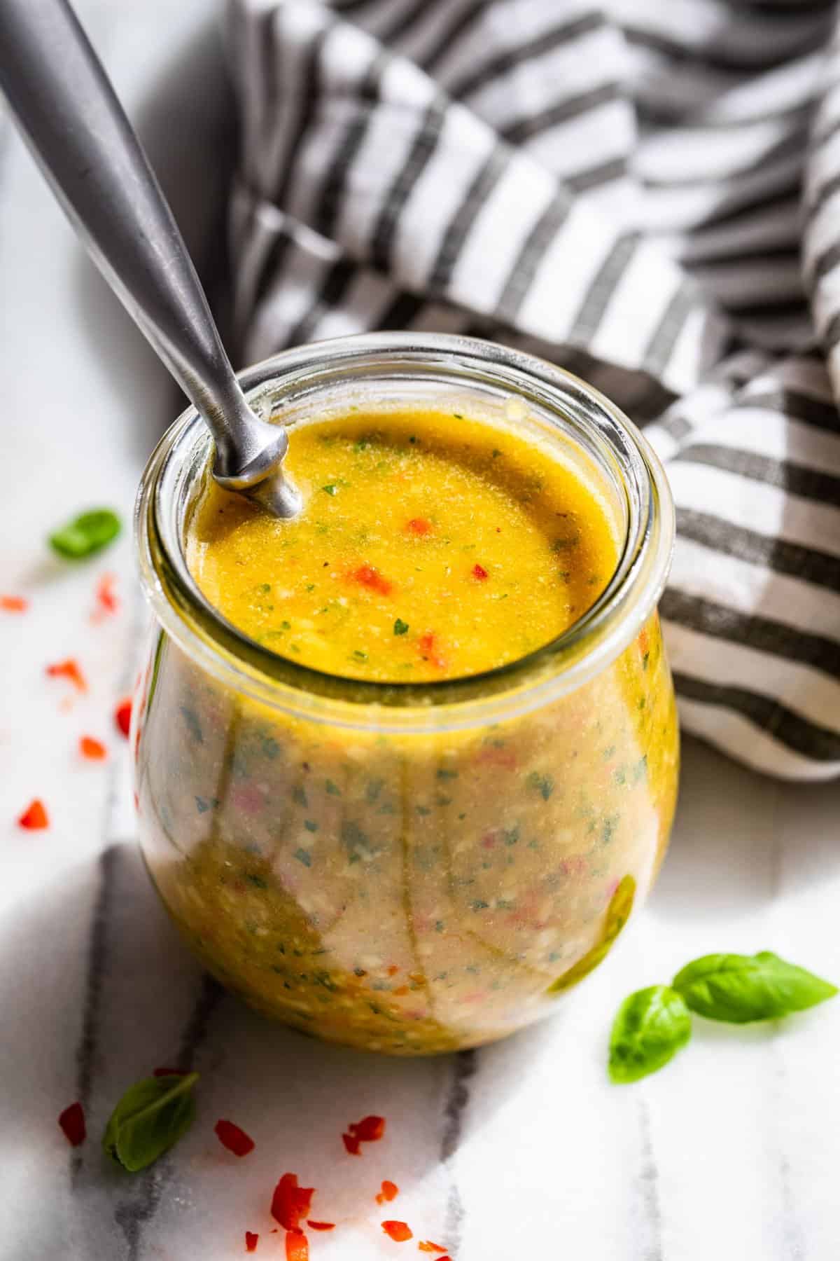 Looking down into a clear glass jar filled with Italian Dressing with a black and white striped linen in the background.