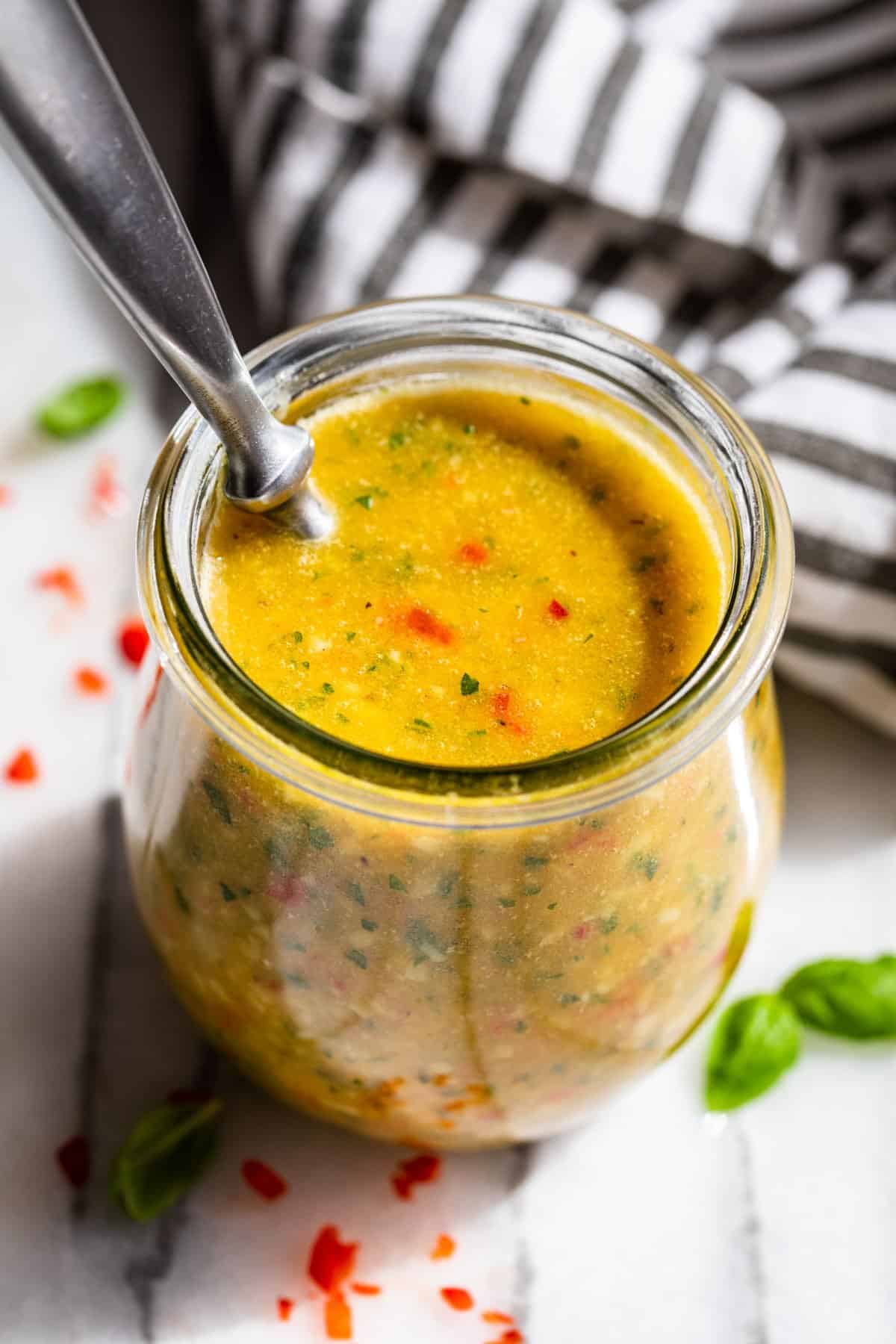 Downwards view of Italian Dressing in a clear glass jar with a spoon in the jar and diced bell pepper around it.