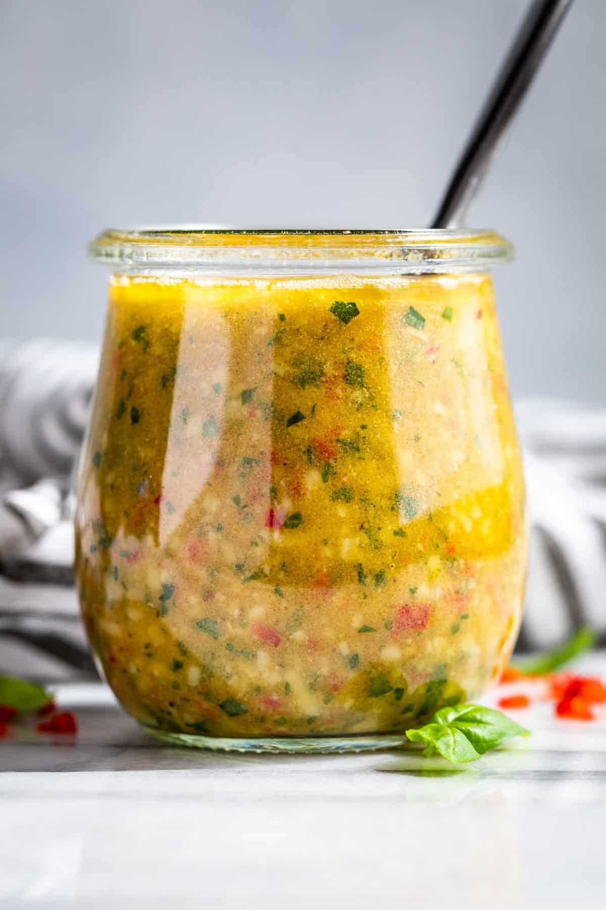 A clear glass jar filling with Homemade Italian Dressing with a silver spoon in it.