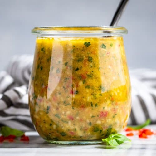 Finished Italian Dressing in a clear glass jar with a silver spoon in the jar.