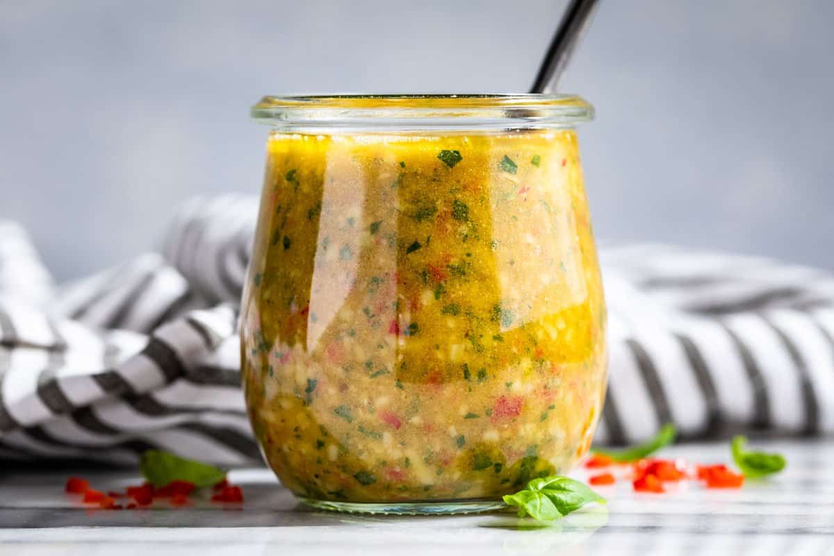 Finished Italian Dressing in a clear glass jar with a silver spoon in the jar.