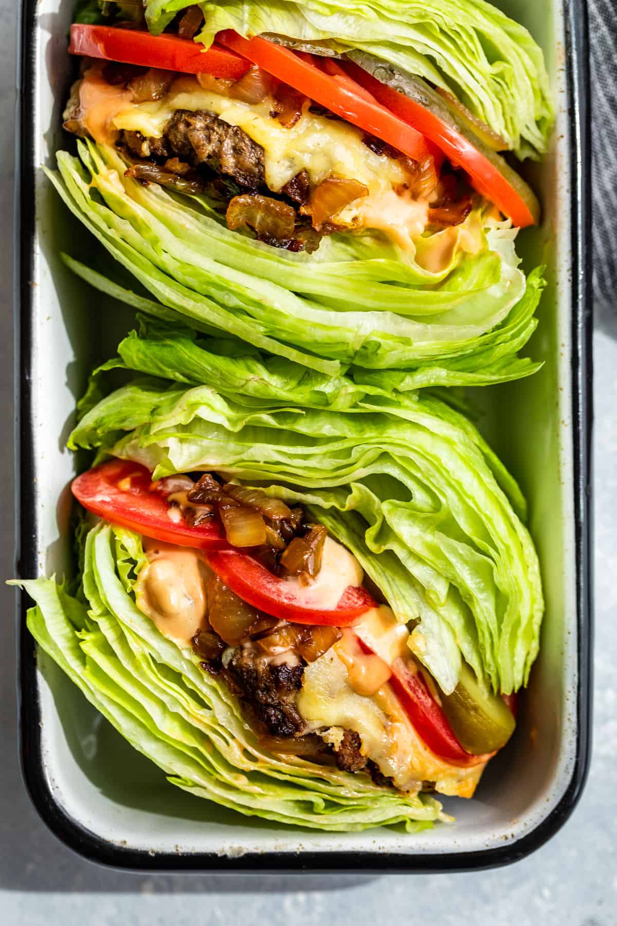 Straight down view of 2 In and Out Burger Lettuce wraps in a black rimmed white enameled container.