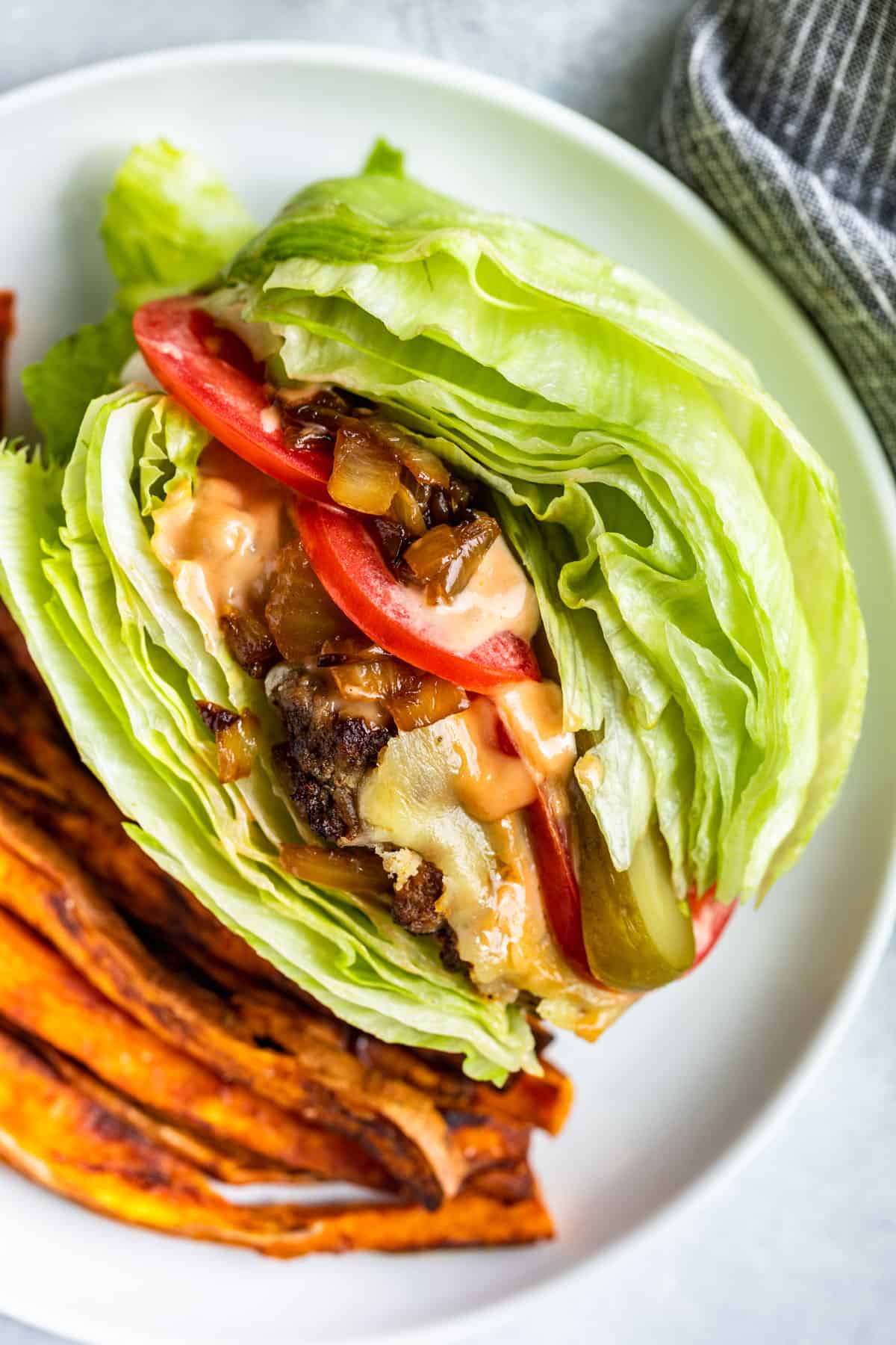 Straight down view of a In and out Burger Lettuce Wrap on a white plate with a side of sweet potato fries.