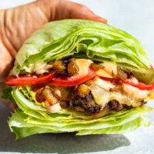 A hand holding a In and Out Burger Lettuce Wrap on a blue background.