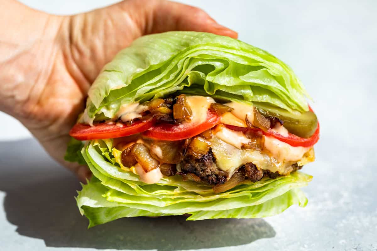 A hand holding a In and Out Burger Lettuce Wrap on a blue background.
