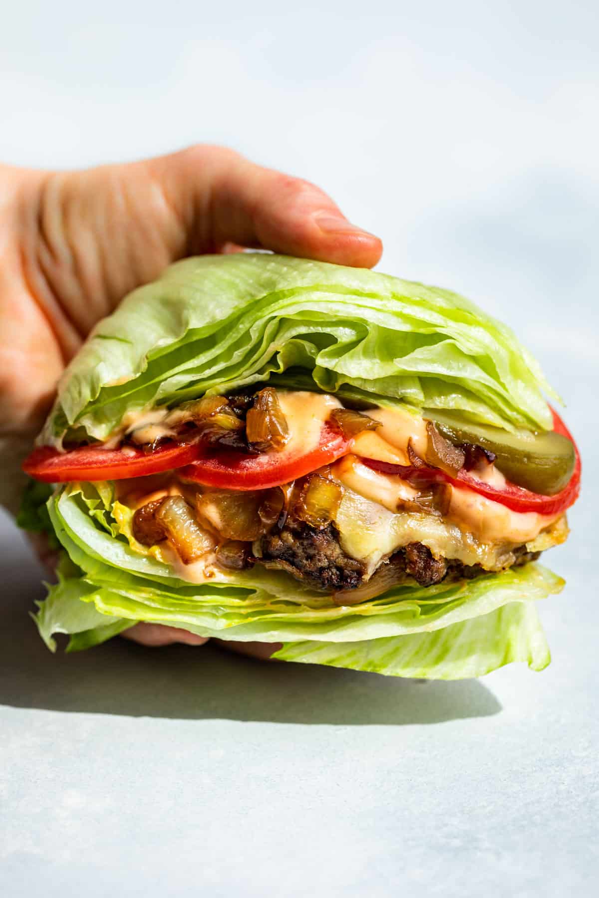 A hand holding a In and Out Burger Lettuce Wrap against a blue background.