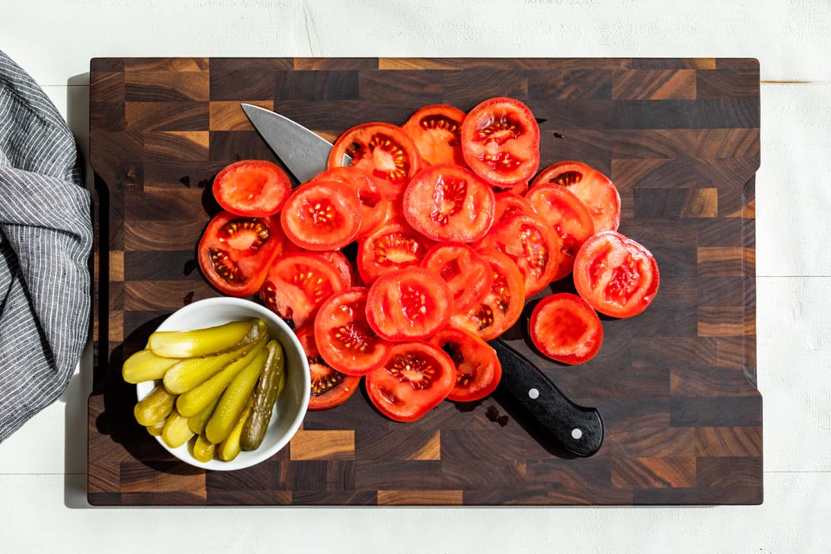 Sliced tomatoes and pickles on a wood cutting board.