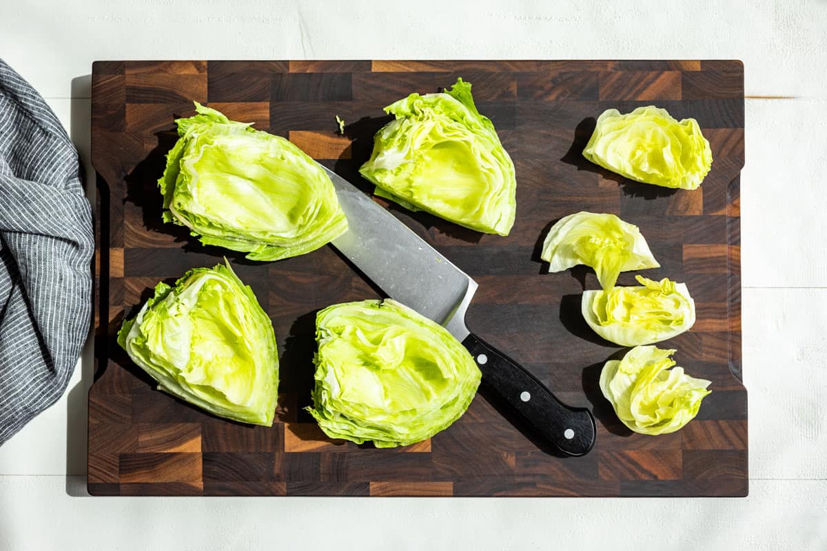 Quartered iceberg lettuce for 'lettuce buns' on a wood cutting board.