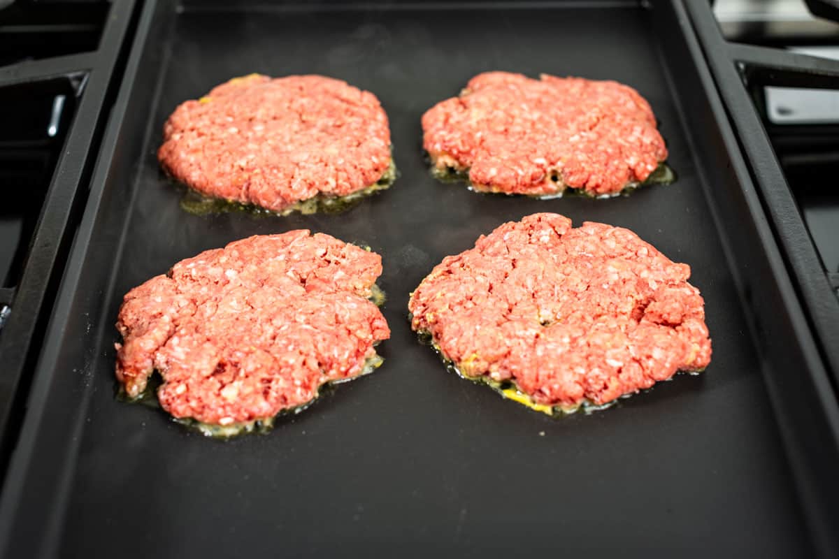 Searing the burger patties mustard side down on a griddle.
