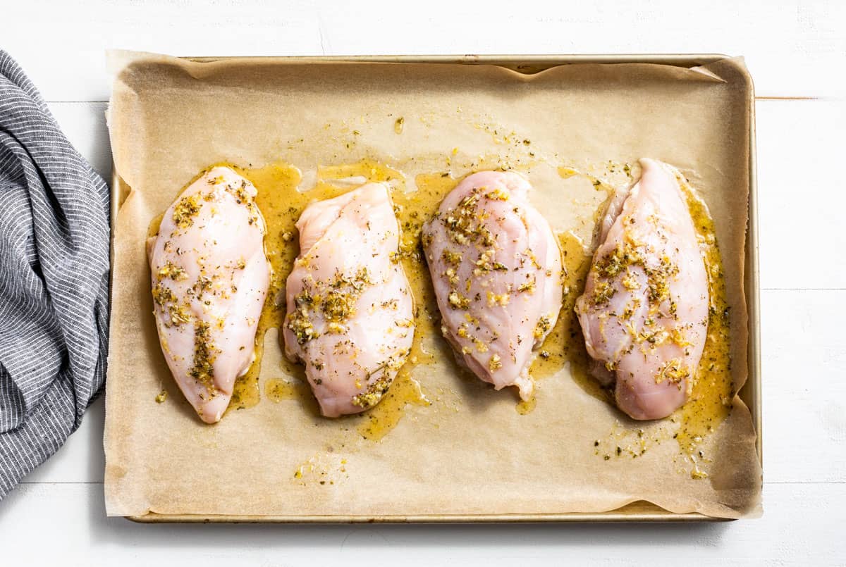 Four chicken breasts on a baking sheet with the Herbs de Provence olive oil mixture.