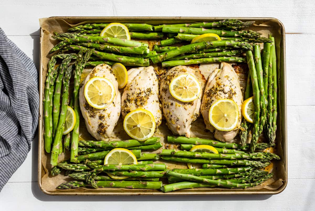 Adding the asparagus and lemon slices to the sheet pan with the partially cooked chicken.