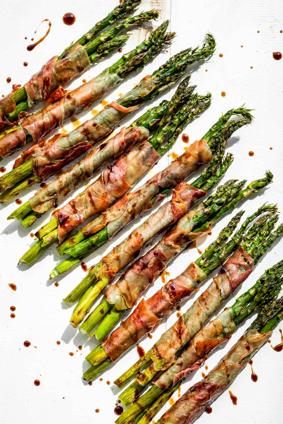 Prosciutto Wrapped Asparagus spears on a white background drizzled with aged balsamic vinegar.