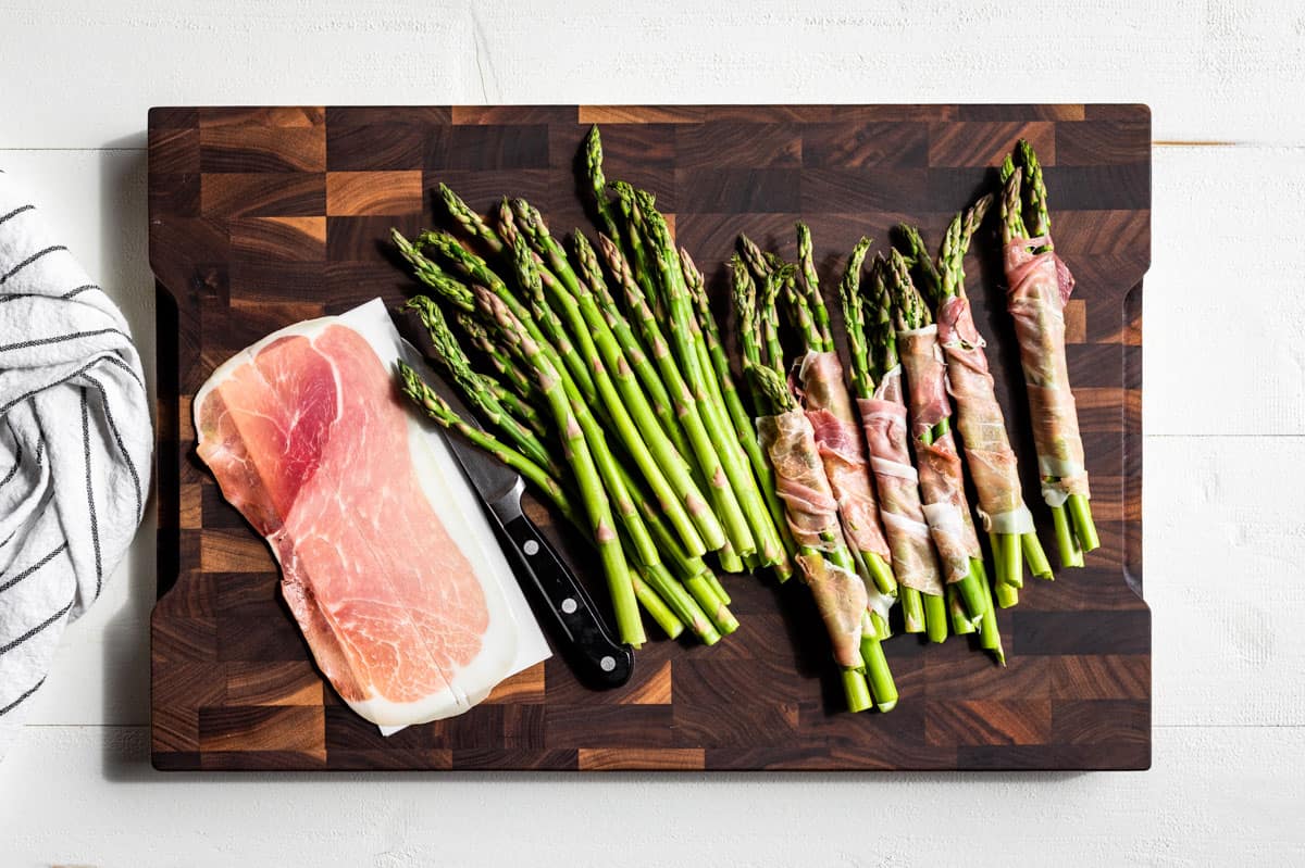 Wrapped the asparagus with prosciutto slices on a wood cutting board.