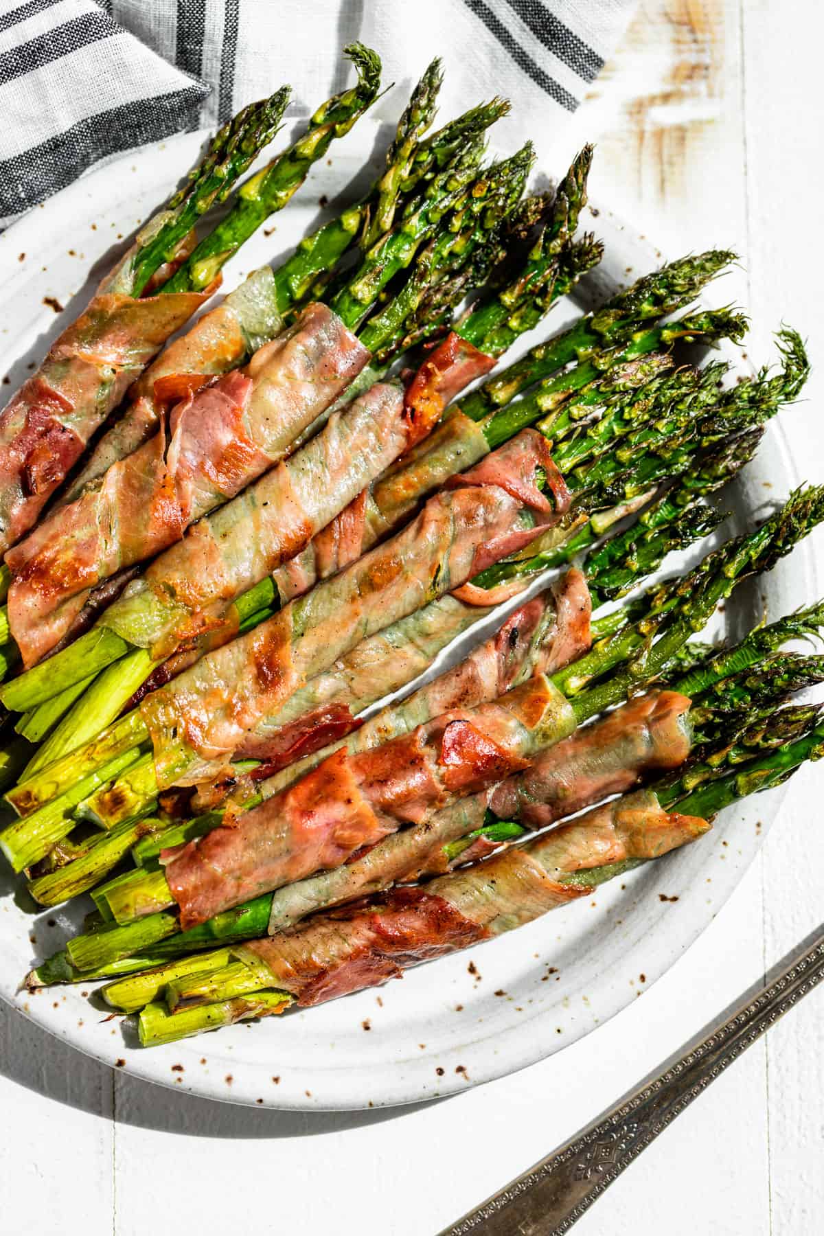 Looking down at Prosciutto Wrapped Asparagus spears arranged on a speckled pottery plate.