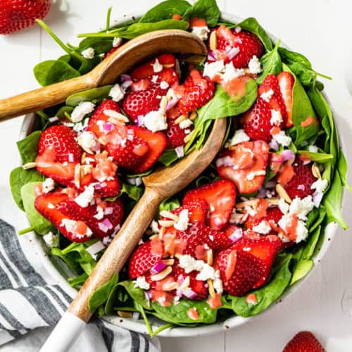 Straight down view of the finished Strawberry Spinach Salad with strawberries around it and a jar of strawberry vinaigrette on the side.
