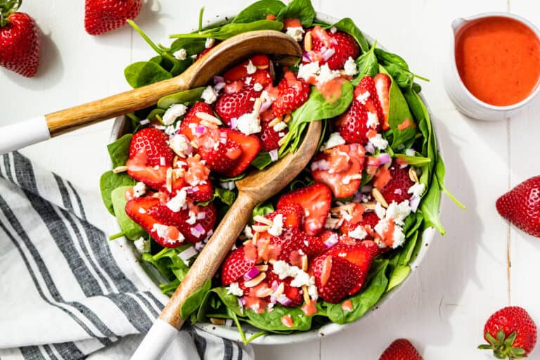 Straight down view of the finished Strawberry Spinach Salad with strawberries around it and a jar of strawberry vinaigrette on the side.