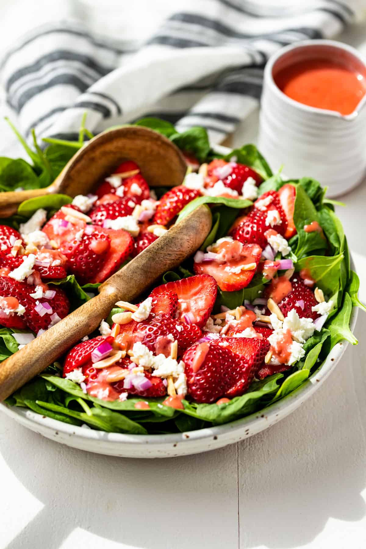 Side view of Strawberry Spinach Salad in a white bowl with a jar of strawberry vinaigrette on the side.