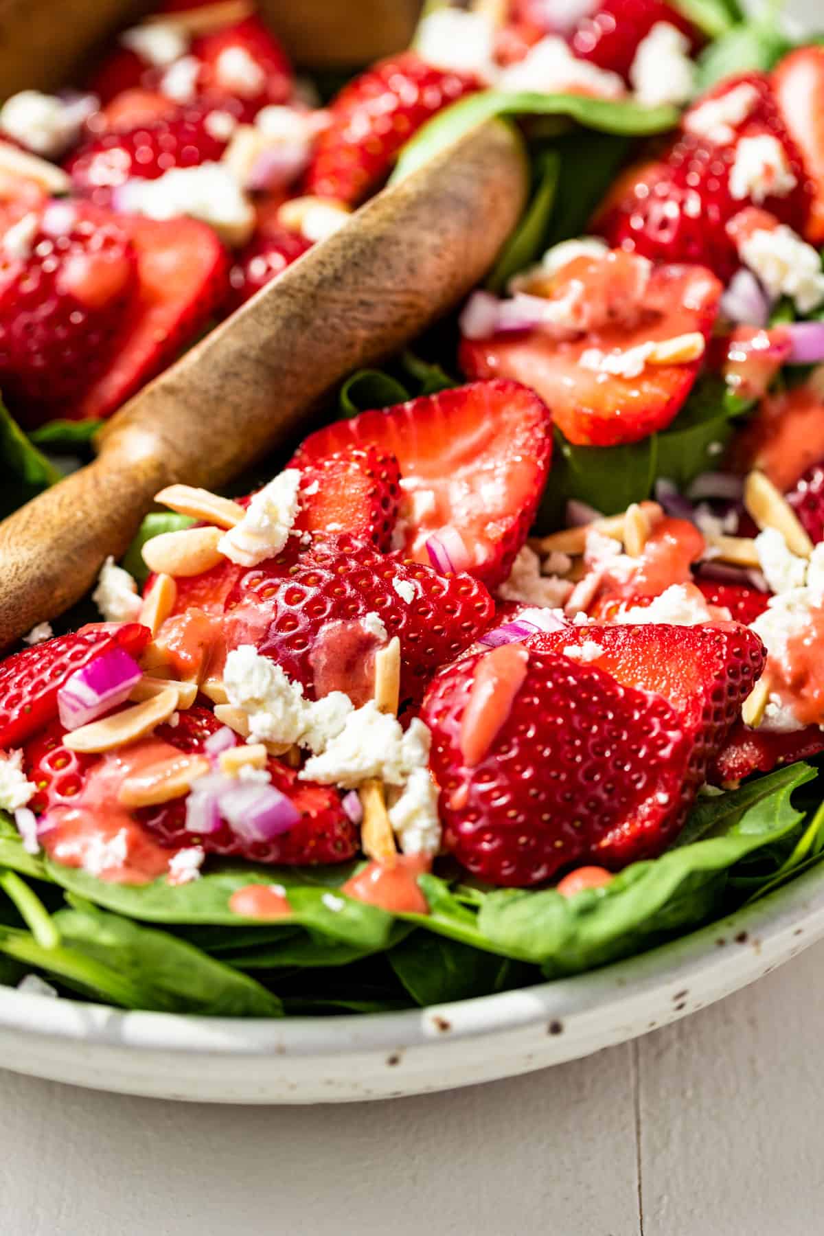 Close macro view of the Strawberry Spinach Salad with a wooden serving spoon scooping in.