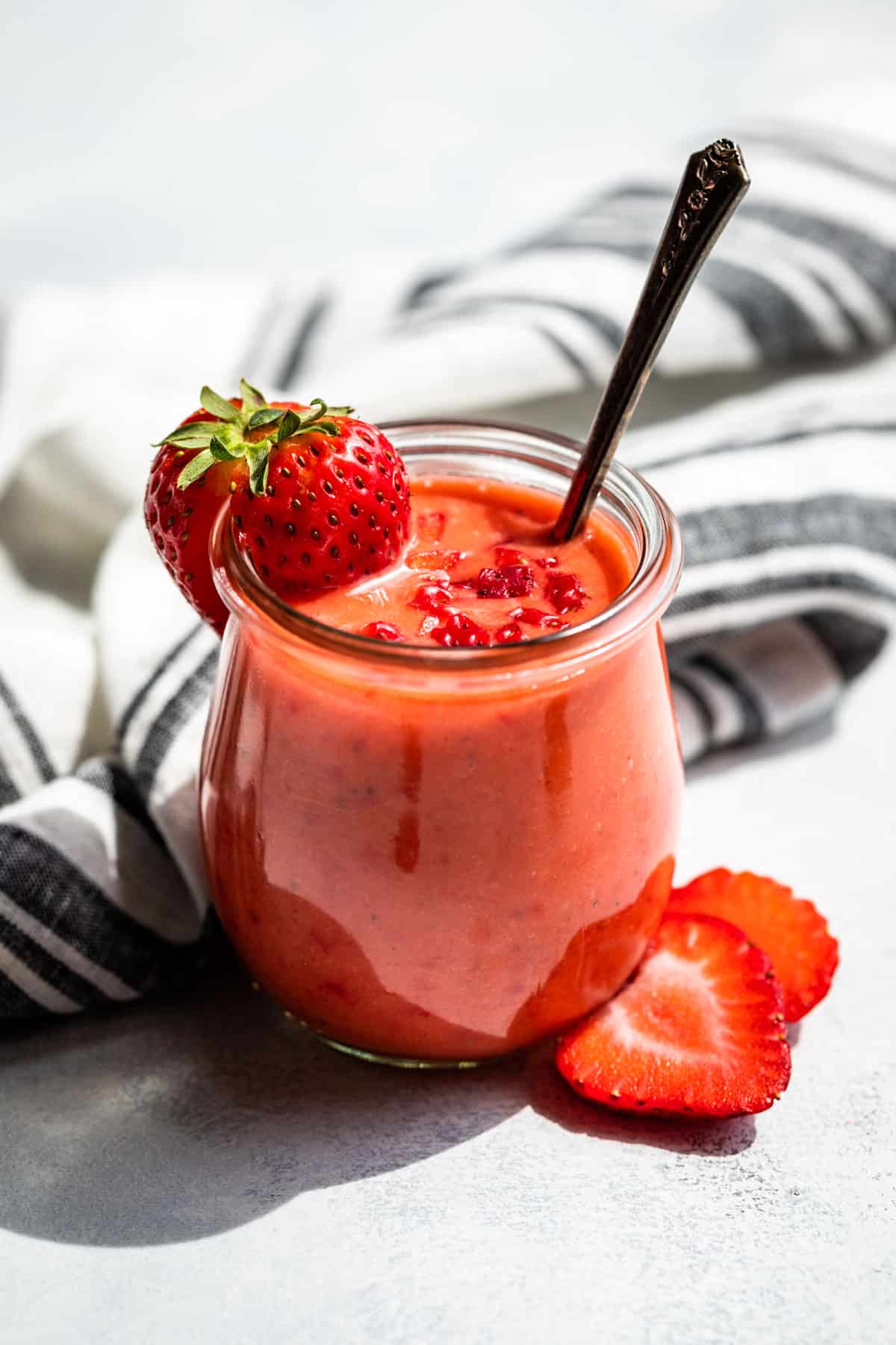 Side view of Strawberry Vinaigrette in a clear glass jar with a silver spoon and a strawberry garnish.