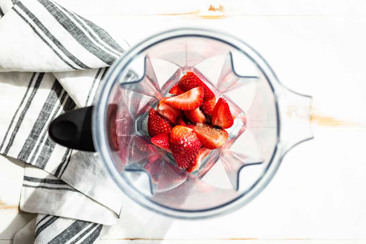 The cut up strawberries, sea salt, pepper, and white wine vinegar in a blender container.
