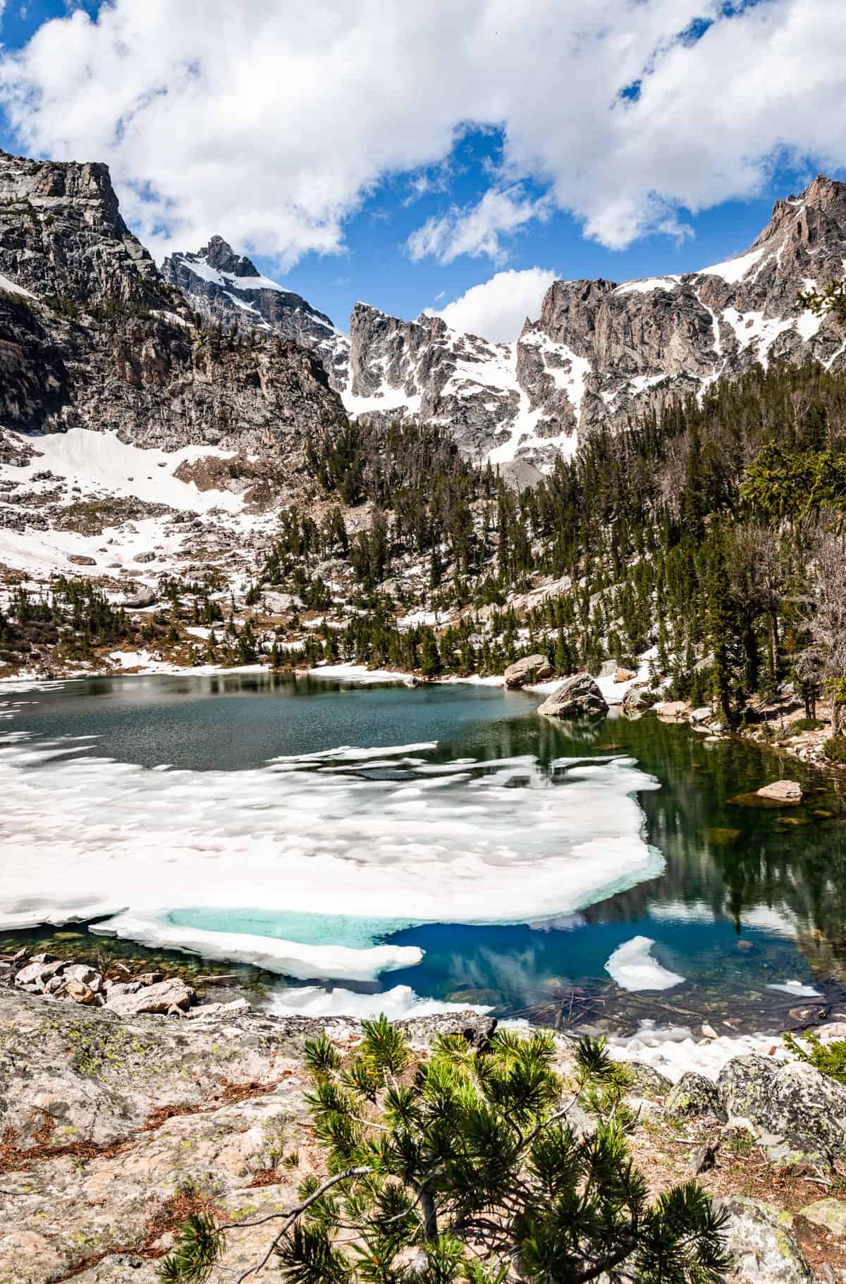 Grand Teton mountains with a partially frozen deep blue lake in the foreground.