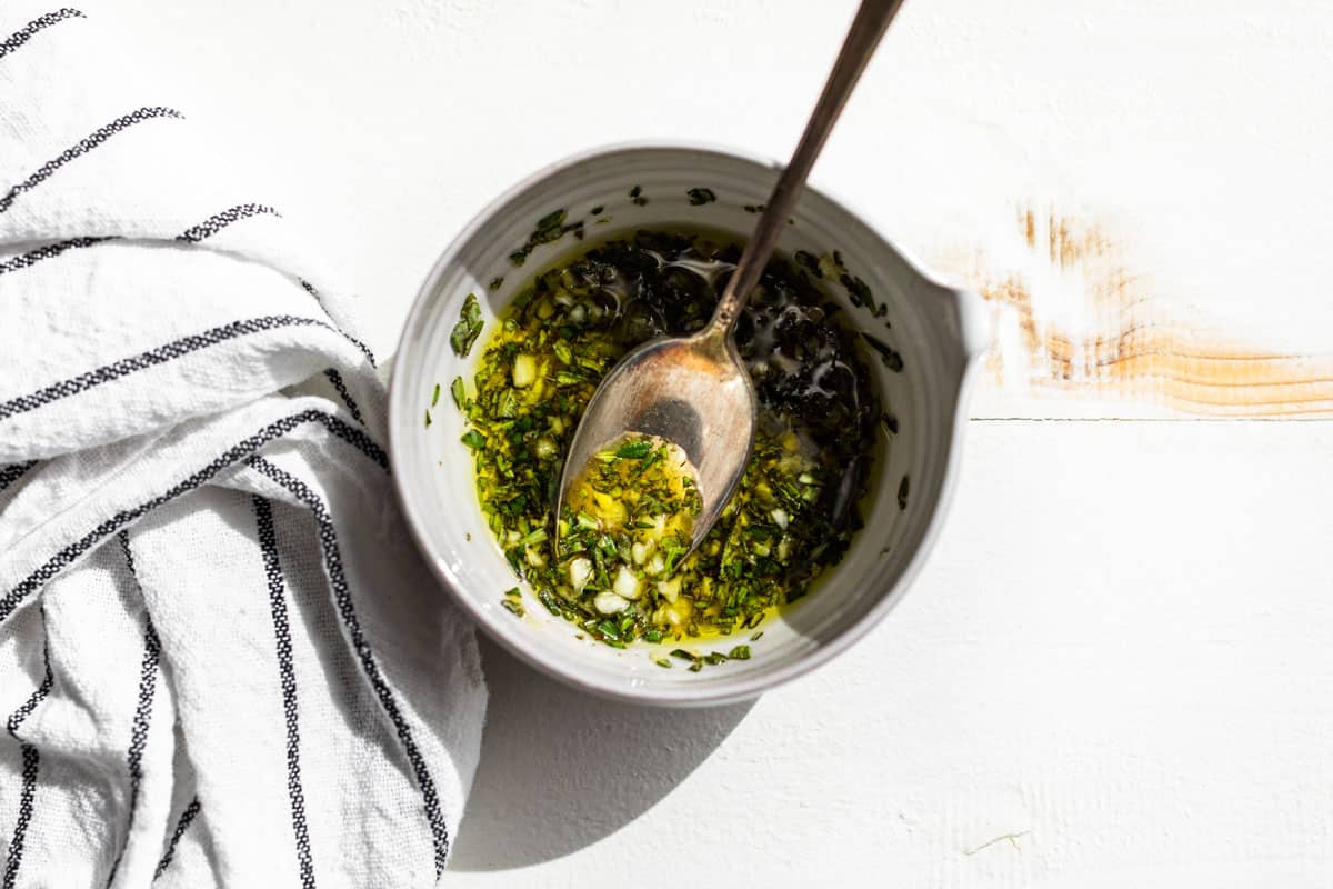 Chopped rosemary, garlic, and olive oil being mixed together in a small pottery bowl.