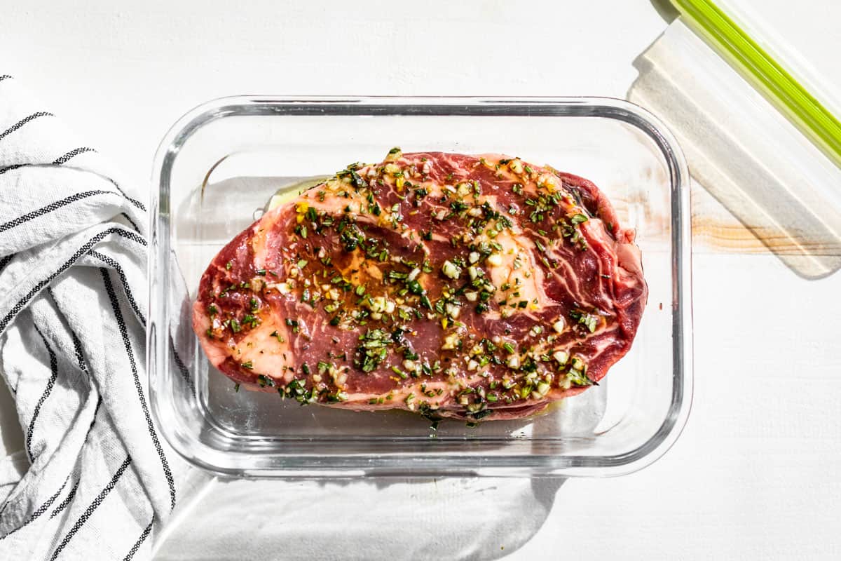 Rosemary olive oil marinade being poured over ribeye steaks in a glass container to marinate.