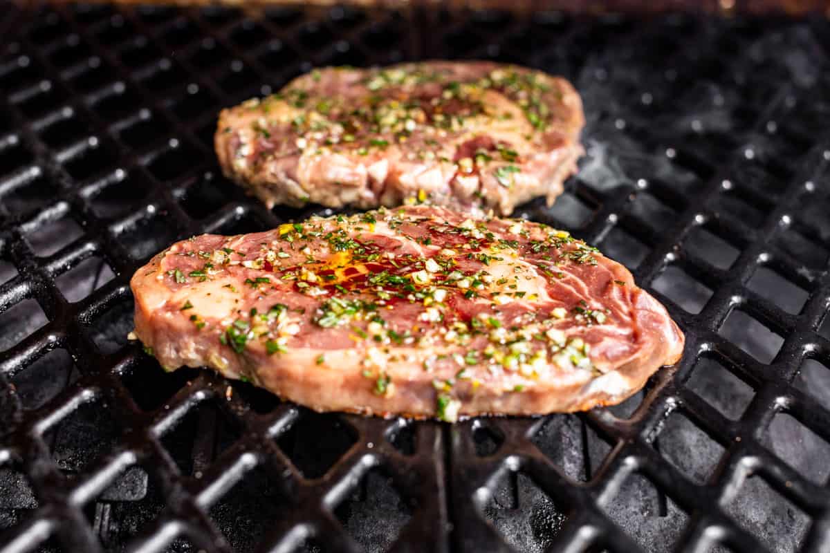 Marinated ribeye steaks being added to a grill.